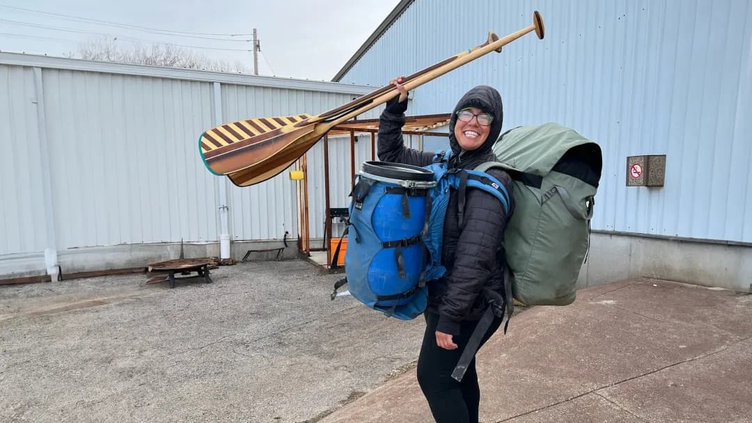 Cory Maria Dack holds her oars in the air with a large pack on her back
