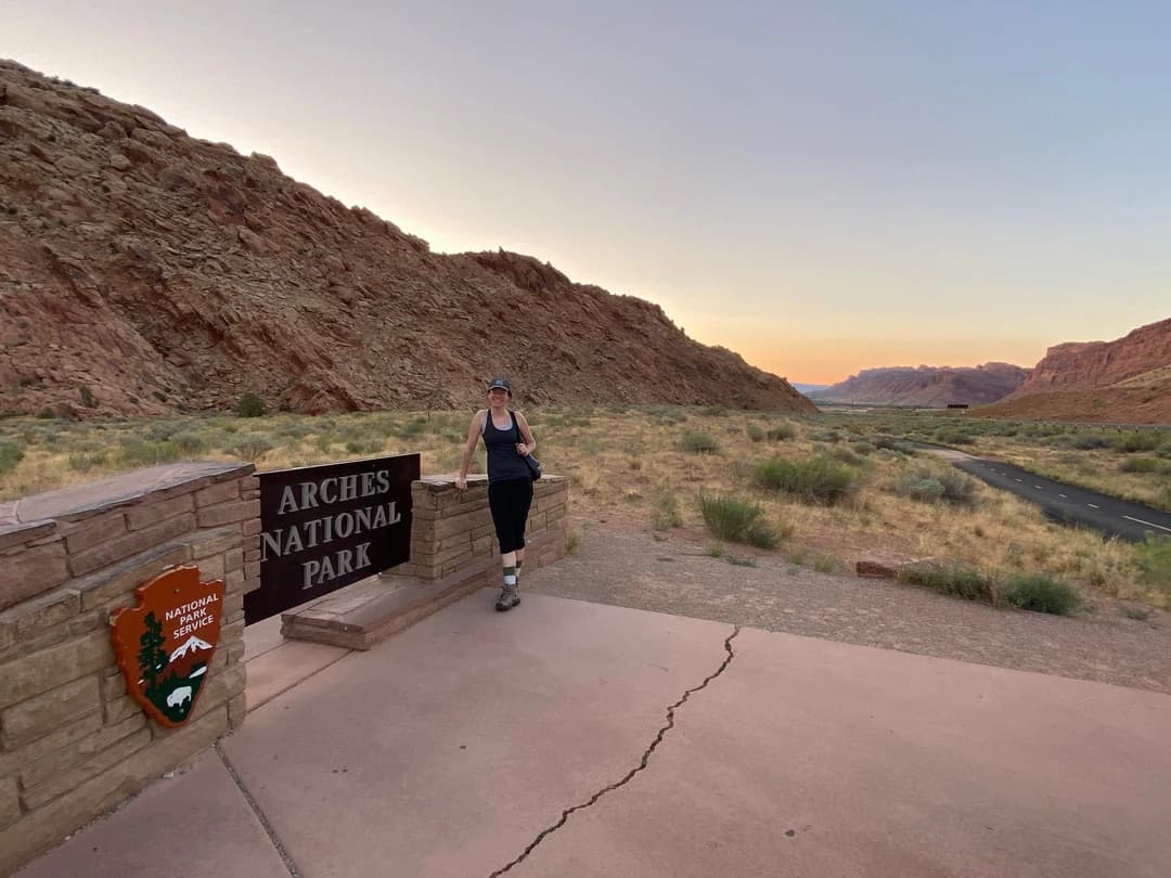 a woman in front of the sign for Arches National Park