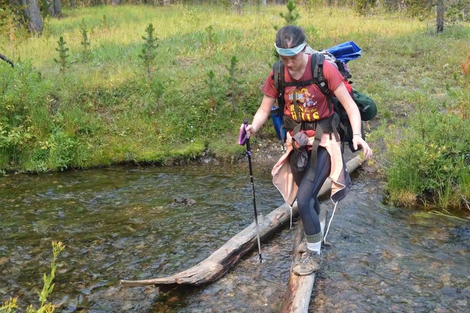 a hiker using walking sticks to get across a stream.