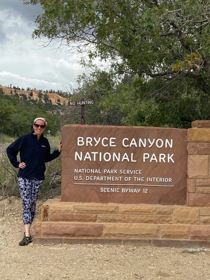 a woman in front of the bryce canyon national park sign