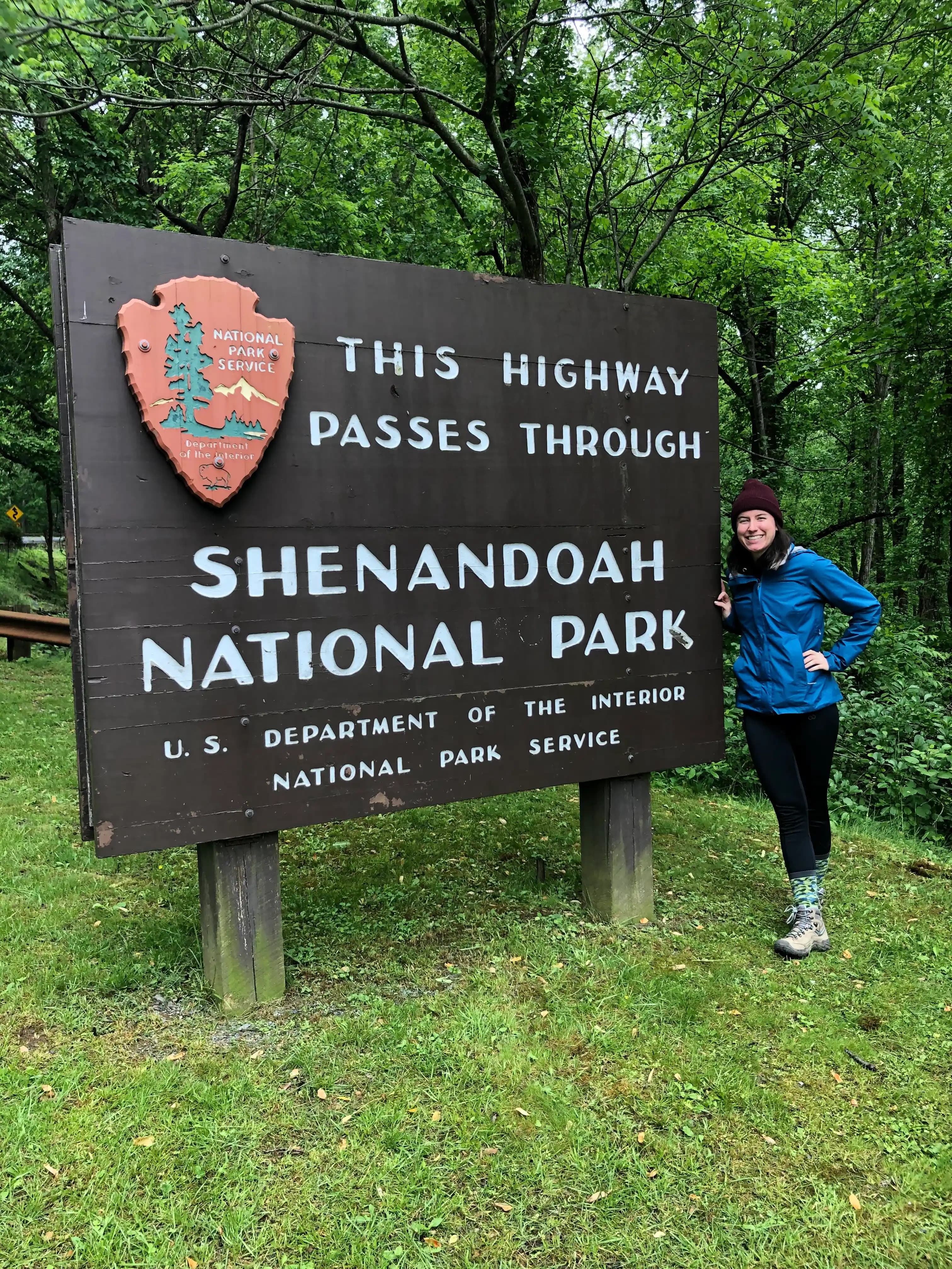 a woman standing in front of the shenandoah national park entrance sign