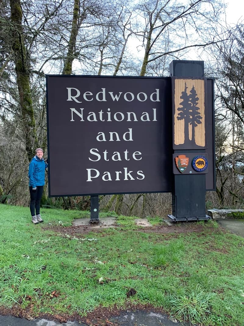 redwood national and state park sign with a woman next to it