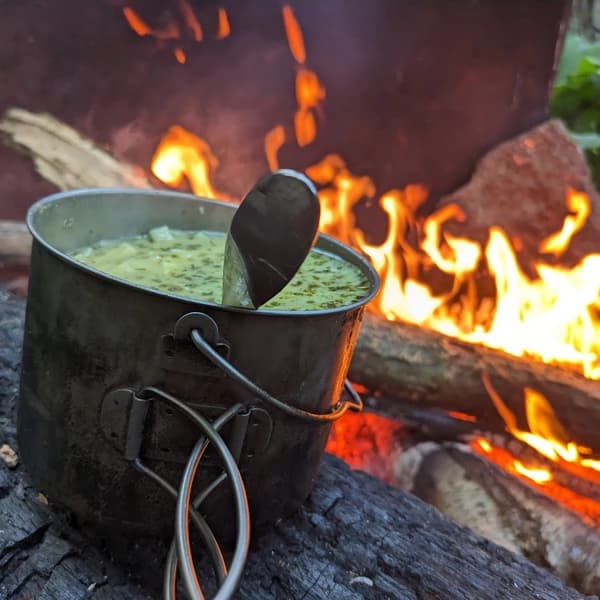 a cup of soup next to a campfire