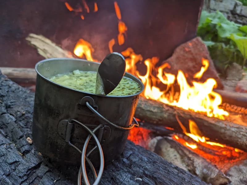 a cup of soup next to a campfire