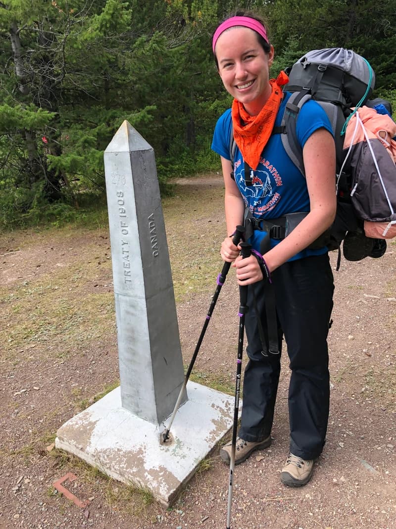 woman standing next to waterton dividing line between us and canada