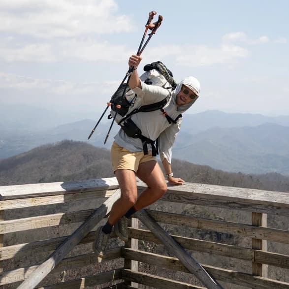 Caleb Adcock hiking on a wooden lookout with mountains in the background